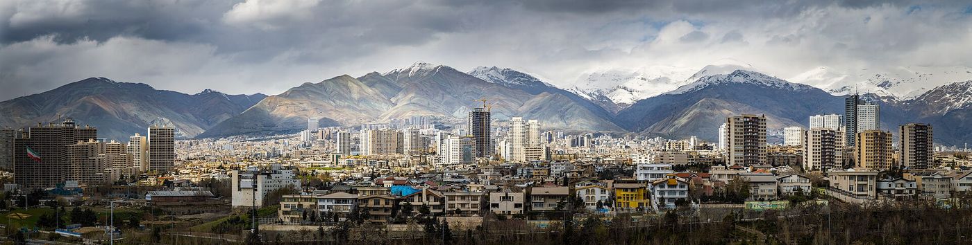 Power lines and apartment towers in Tehran, with the Alborz mountains behind, in a city facing scheduled electricity outages.
